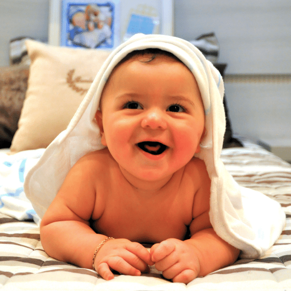 A foto mostra um bebê que acabou de sair do banho com uma toalhinha na cabeça, ele está todo sorridente.