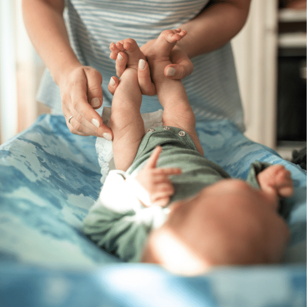 A foto mostra uma mãe trocando a fralda descartável do seu bebê.