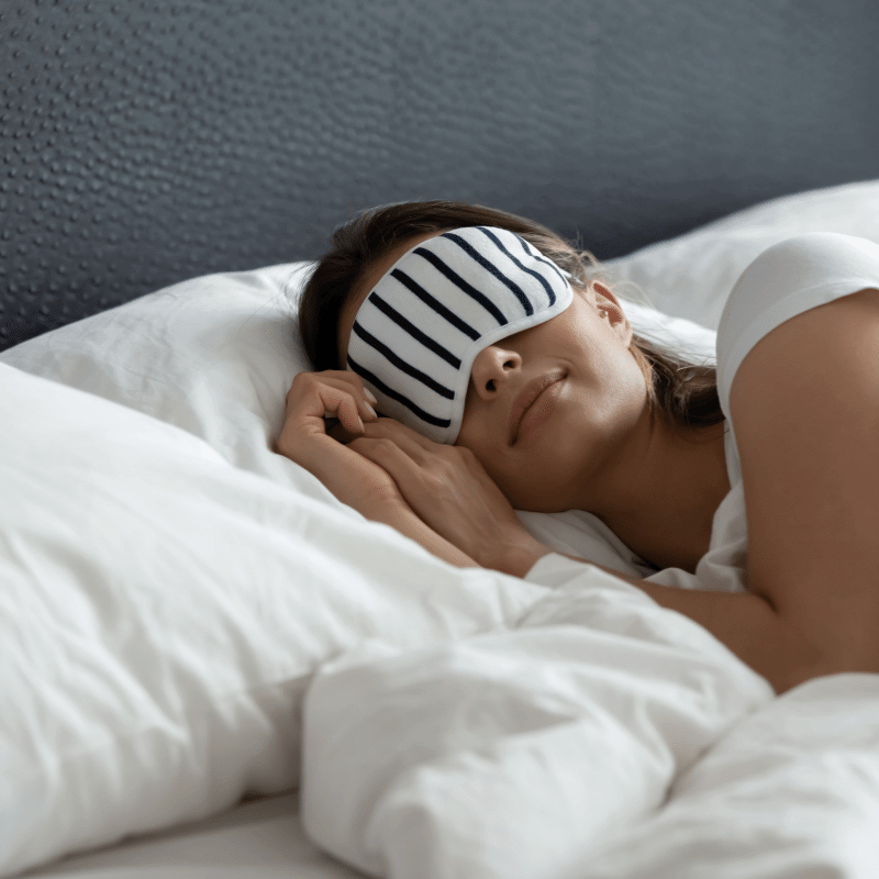 A foto mostra uma mulher dormindo numa cama confortável e ela está usando proteção nos olhos.
