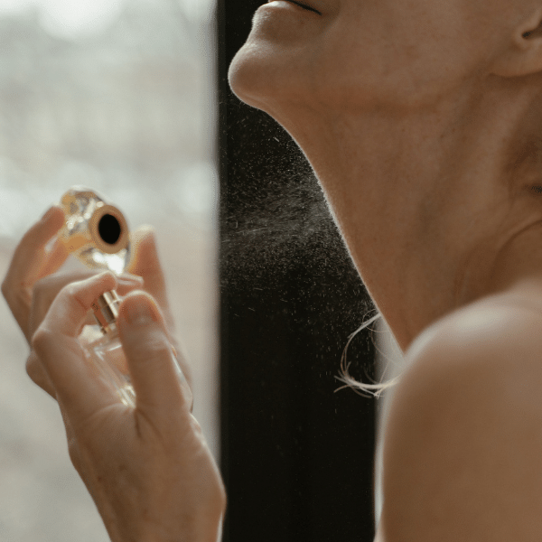 A imagem mostra uma mulher borrifando perfume na região do pescoço.