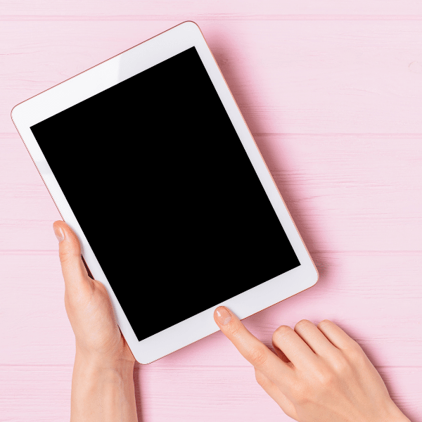 A foto mostra a tela de um tablet na cor branca com duas mãos o segurando.