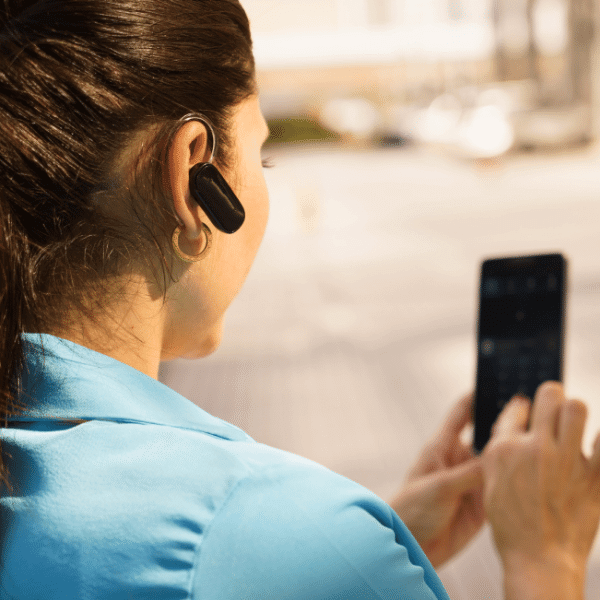 A foto mostra uma mulher mexendo no celular, ela esta utilizando fone de ouvido bluetooth.