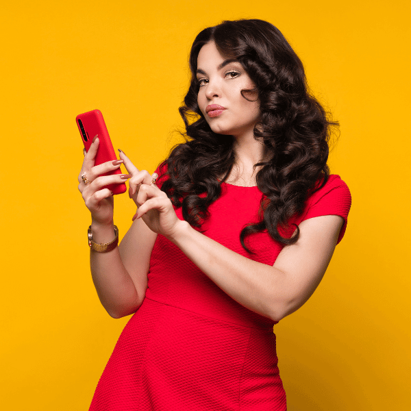 Imagem em fundo amarelho que mostra uma mulher com um vestido vermelho usando um celular com uma capinha vermelha.