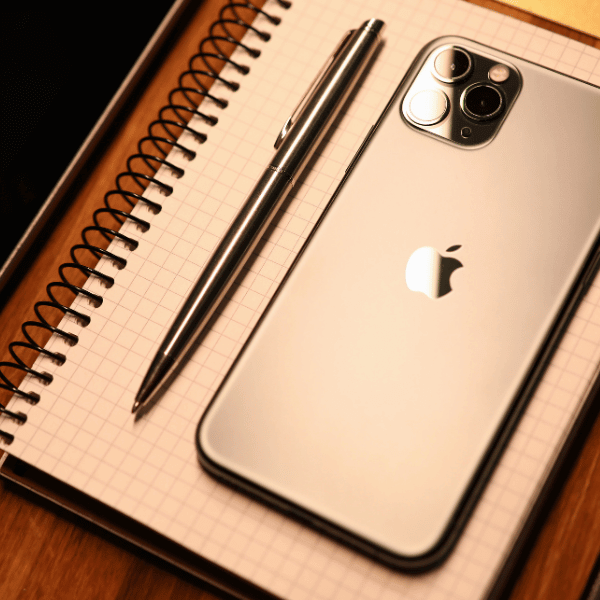 A foto mostra um iPhone e uma caneta em cima de um caderno com linhas quadriculadas.